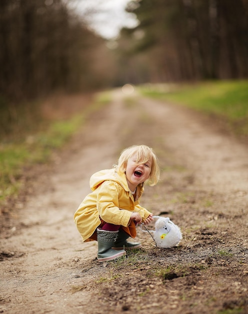 Linda menina holandesa engraçada com um casaco impermeável amarelo e botas brincando no campo