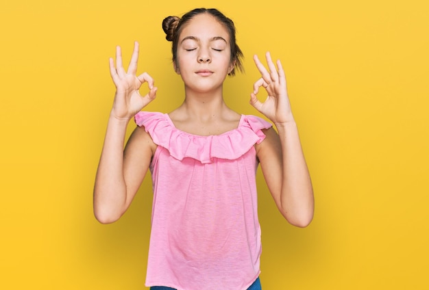 Linda menina morena vestindo camisa rosa de verão relaxar e sorrir com os olhos fechados fazendo gesto de meditação com os dedos. conceito de ioga.