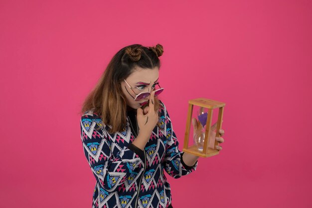 Linda menina segurando o relógio de areia e usando óculos olhando para o lado. Foto de alta qualidade