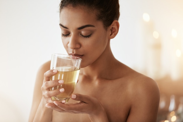 Linda mulher africana bebendo chá sorrindo relaxante no salão spa.