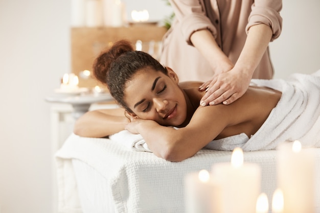 Linda mulher africana sorrindo desfrutando de massagem com os olhos fechados no salão spa.