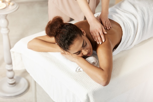 Foto grátis linda mulher africana sorrindo desfrutando de massagem com os olhos fechados no salão spa.