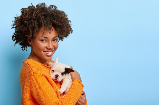 Linda mulher afro-americana fica de lado, brinca com o cachorrinho bulldog em casa, mostra amor entre o dono e o animal de estimação