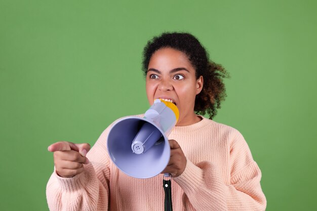 Linda mulher afro-americana na parede verde gritando e gritando no megafone, pedindo atenção