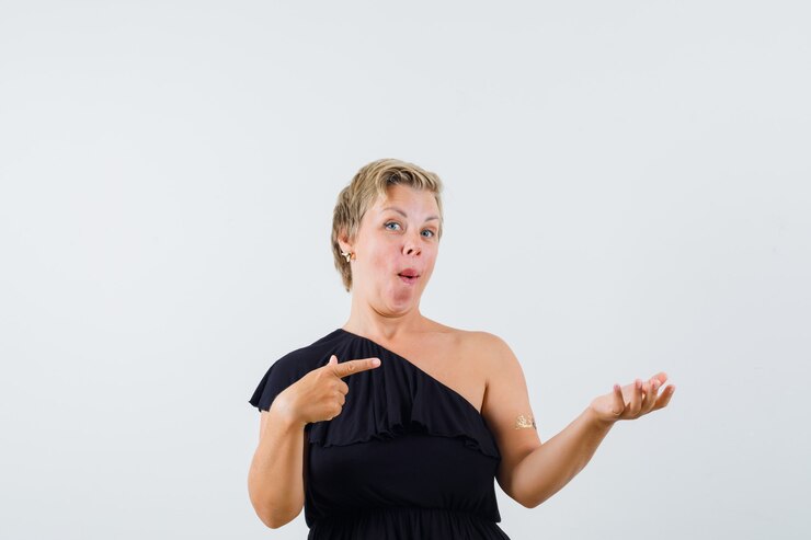 Foto grátis linda mulher apontando para o lado enquanto levanta a mão com a palma aberta de lado na blusa preta e parecendo surpresa.