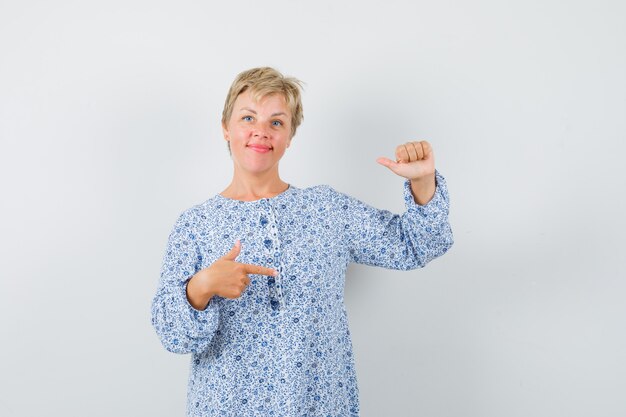 Linda mulher apontando para o lado na blusa estampada e olhando concentrada, vista frontal.