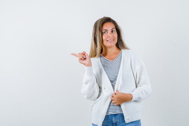 Linda mulher apontando para o lado na jaqueta e parecendo confusa, vista frontal.