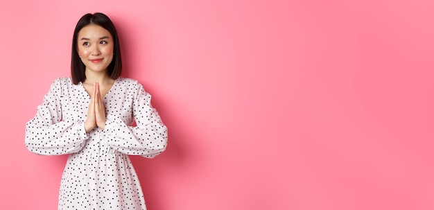 Foto grátis linda mulher asiática angelical sorrindo de mãos dadas em oração e olhando para a esquerda no espaço da cópia com inno