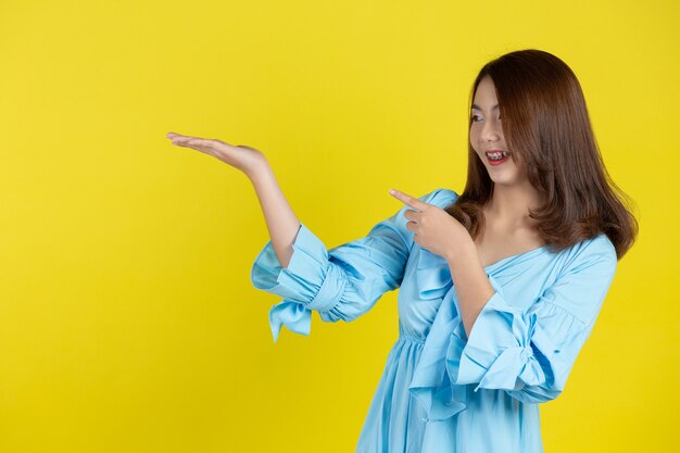 Linda mulher asiática apontando a mão para o espaço vazio ao lado na parede amarela