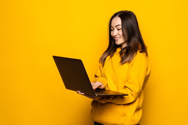 Foto grátis linda mulher asiática estudando no laptop e sorrindo, encostada na parede amarela