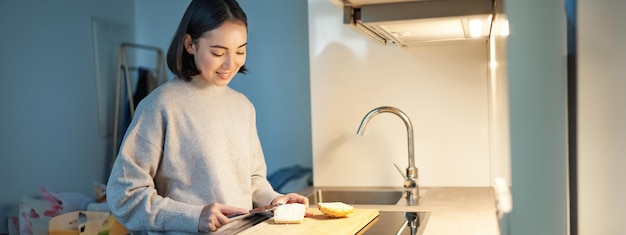 Foto grátis linda mulher asiática fazendo torradas cortando pão preparando sanduíche na cozinha