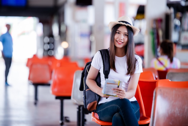 Linda mulher asiática sorrindo com mapa e bolsa na estação de ônibus