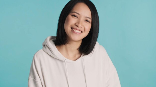 Linda mulher asiática vestida com capuz branco sorrindo para a câmera sobre fundo azul mulher posando no estúdio