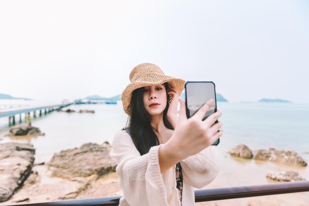 Linda mulher asiática vestindo maiô faz uma selfie na praia no verão de férias