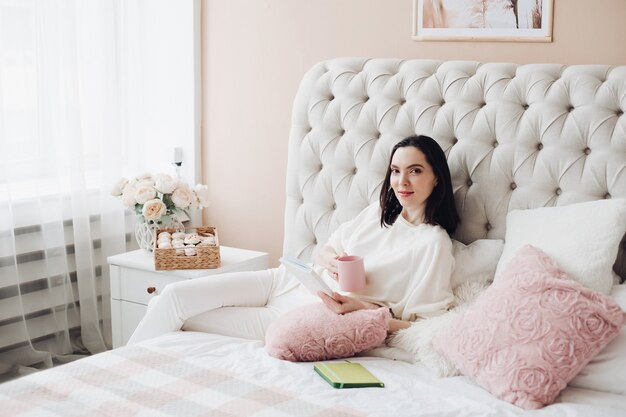 Linda mulher caucasiana deita-se na cama grande e iluminada e pensa em seus planos para o futuro