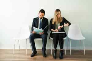 Foto grátis linda mulher caucasiana olhando para o relógio e esperando uma entrevista de emprego. homem latino e mulher de terno em um escritório de recrutamento