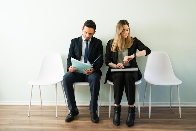 Linda mulher caucasiana olhando para o relógio e esperando uma entrevista de emprego. Homem latino e mulher de terno em um escritório de recrutamento