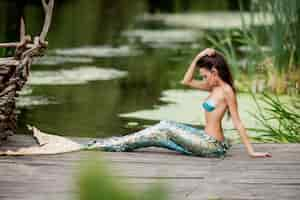 Foto grátis linda mulher com cabelos longos e vestida como uma sereia senta-se na ponte sobre a água