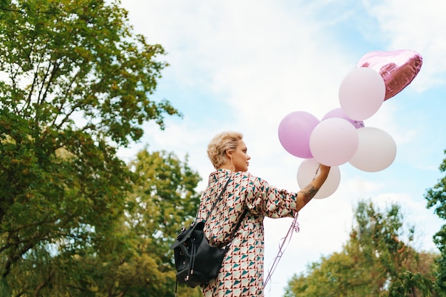 Linda mulher com mochila andando feliz com balões cor de rosa no parque. Liberdade e conceito de mulheres saudáveis.