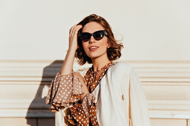 Linda mulher com roupa vintage, expressando interesse. Foto ao ar livre de glamourosa garota feliz em óculos de sol.
