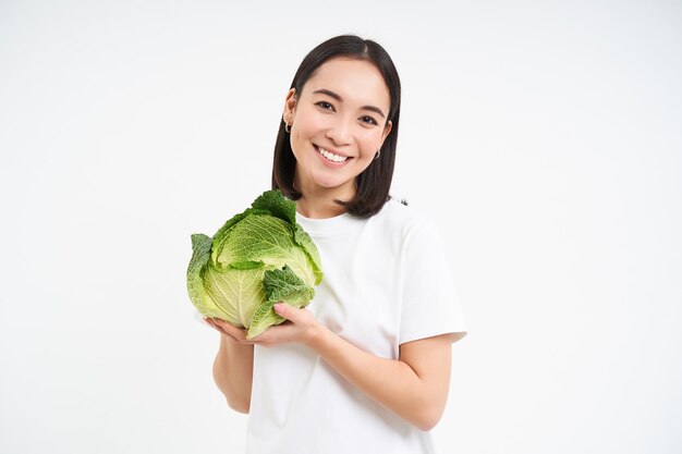 Linda mulher coreana segurando repolho e sorrindo isolado no fundo branco do estúdio