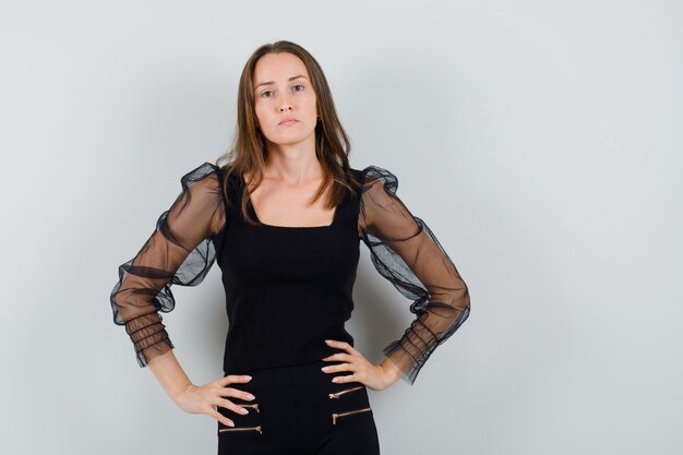 Linda mulher de blusa preta de mãos dadas na cintura e olhando séria