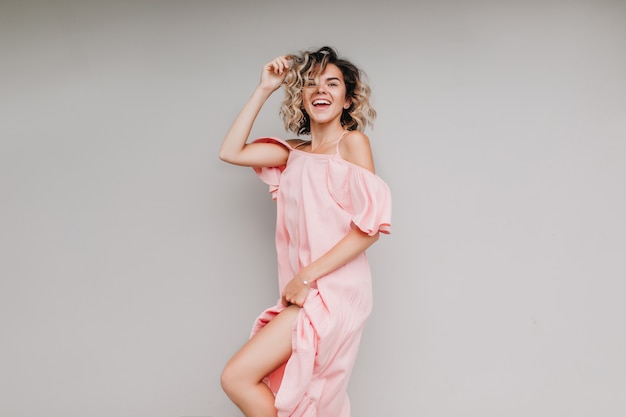 Linda mulher de cabelos curtos em um vestido rosa sorrindo. Adorável menina loira com roupa romântica, expressando energia.