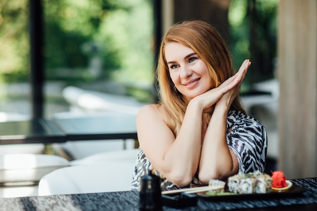 Linda mulher de meia-idade no terraço do café com um prato de rolinhos de sushi