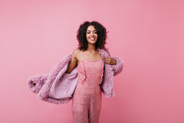 Foto grátis linda mulher dos eua está vestindo seu novo casaco de lama. retrato interior da menina da risada com um estilo de cabelo volumoso.