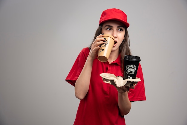 Foto grátis linda mulher entregadora de uniforme vermelho, bebendo café.