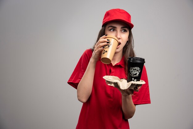Linda mulher entregadora de uniforme vermelho, bebendo café.