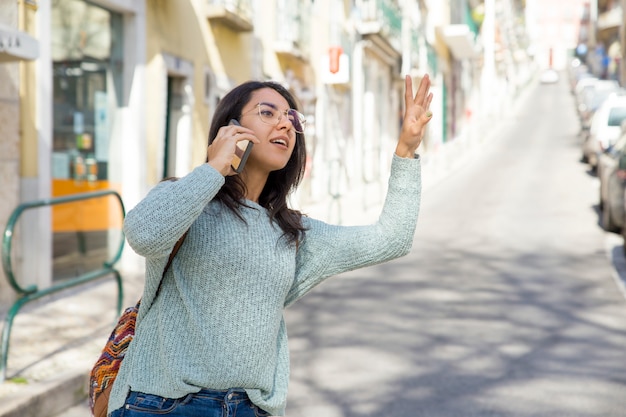 Linda mulher falando no telefone e saudando o táxi