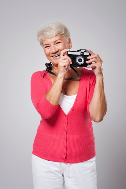 Linda mulher feliz sênior tirando foto com câmera retro