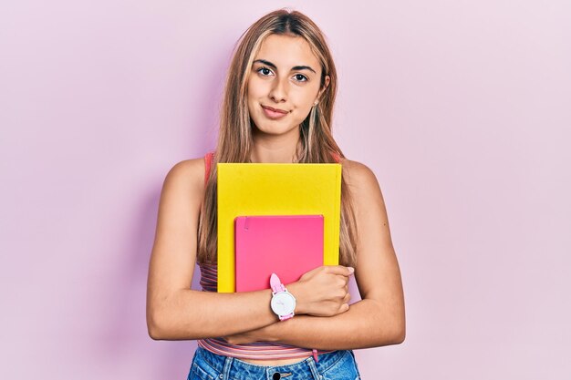 Linda mulher hispânica segurando livros pensando em atitude e expressão sóbria parecendo autoconfiante