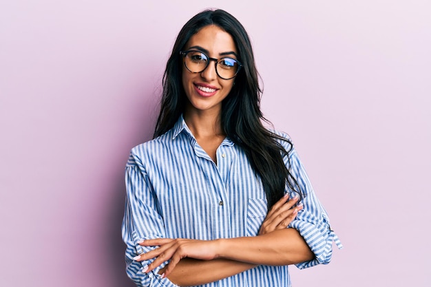 Linda mulher hispânica vestindo roupas casuais e óculos rosto feliz sorrindo com os braços cruzados, olhando para a câmera. pessoa positiva.