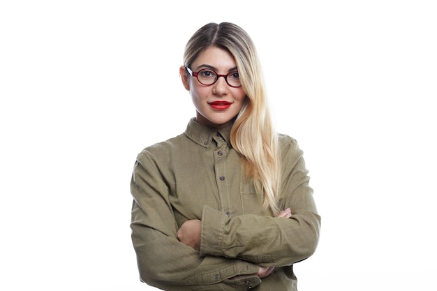 Foto grátis linda mulher jovem e atraente isolada usando óculos da moda, batom vermelho e cabelos soltos coloridos de um lado com um sorriso confiante, mantendo os braços cruzados