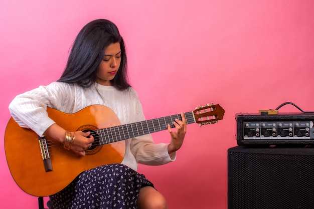 Linda mulher latina tocando violão com uma parede rosa na cena