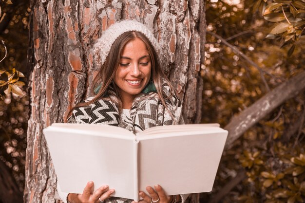 Linda mulher lendo livro perto da árvore