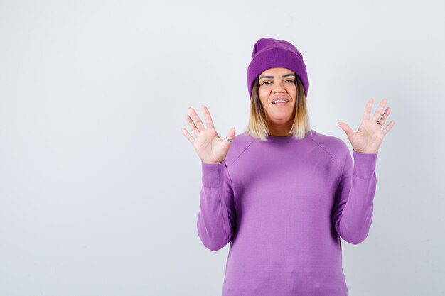 Linda mulher levantando as mãos em gesto de rendição no suéter, gorro e parecendo indefeso. vista frontal.