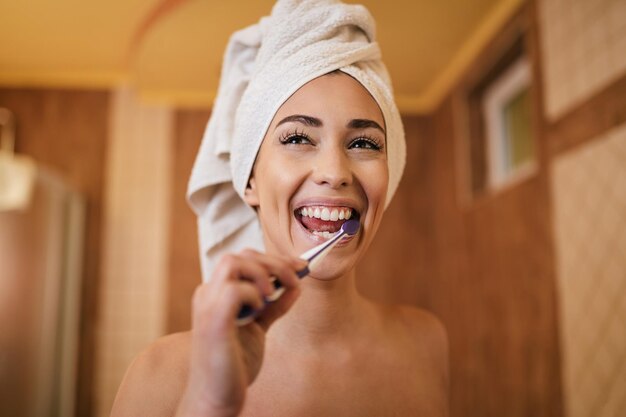 Linda mulher limpando os dentes com uma escova de dentes no banheiro