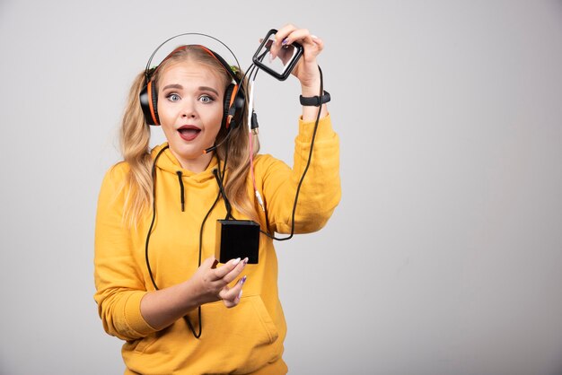 Linda mulher loira mostrando fones de ouvido em fundo cinza.