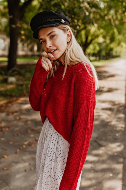 Linda mulher loira posando no parque outono. Linda garota usando um belo chapéu preto com blusa vermelha e saia branca.