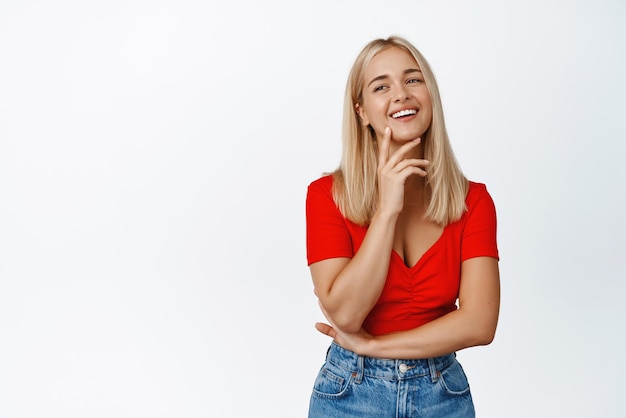 Linda mulher loira rindo sorrindo e parecendo feliz em roupas elegantes contra fundo branco