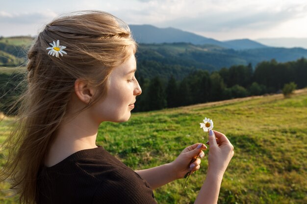 Linda mulher loira segurando para fotos camomiles, fundo de montanhas dos Cárpatos