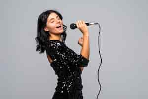 Foto grátis linda mulher morena cantando para o microfone isolado na parede cinza