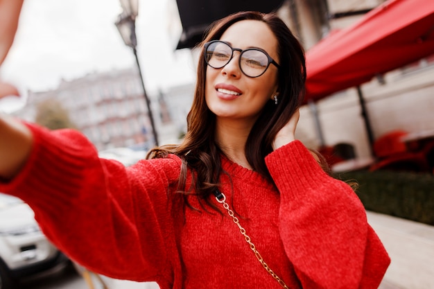 Linda mulher morena com sorriso perfeito, fazendo auto-retrato. vestindo uma camisola de malha vermelha. moda primavera