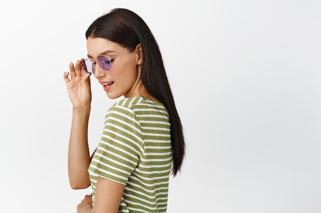 Linda mulher morena em óculos de sol olhando suavemente e feminina em tshirt sobre fundo branco