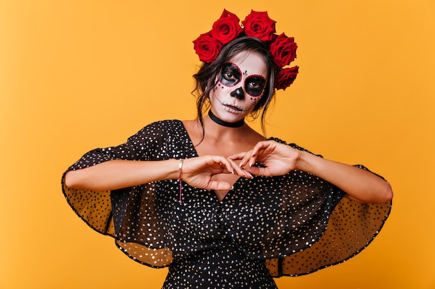 Linda mulher morta posando no halloween na parede amarela. zumbi feminino maravilhoso em coroa de flores rosa.