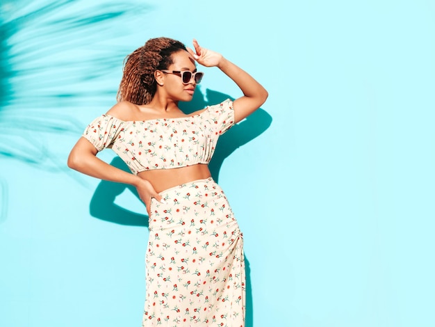 Foto grátis linda mulher negra com penteado de cachos afro modelo sorridente vestido com roupas de verão hipster mulher despreocupada sexy posando perto da parede azul no estúdio bronzeado e alegre em óculos de sol