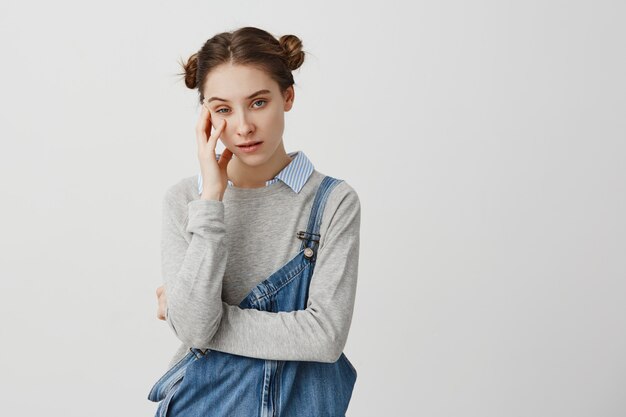 Linda mulher posando com olhar irritado, sendo farto de alguém segurando sua cabeça com a mão. Garota vestindo macacão jeans cansado de ouvir histórias desinteressantes sendo aborrecido. Conceito de emoções